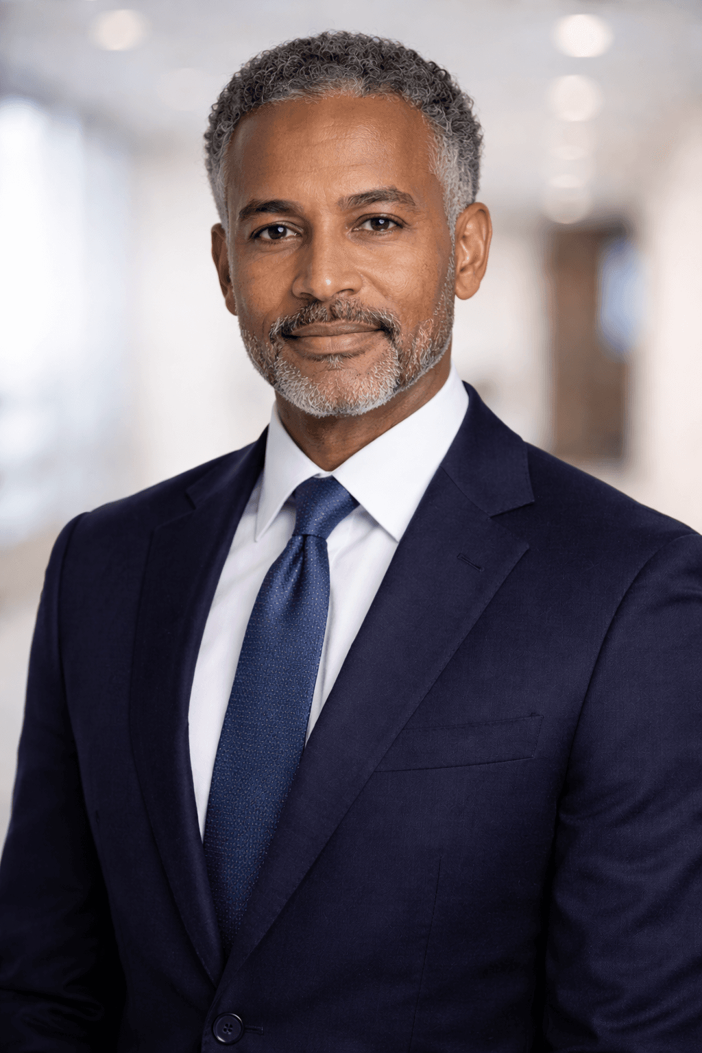 Professional headshot of a Black man with grey hair wearing a navy blue suit.